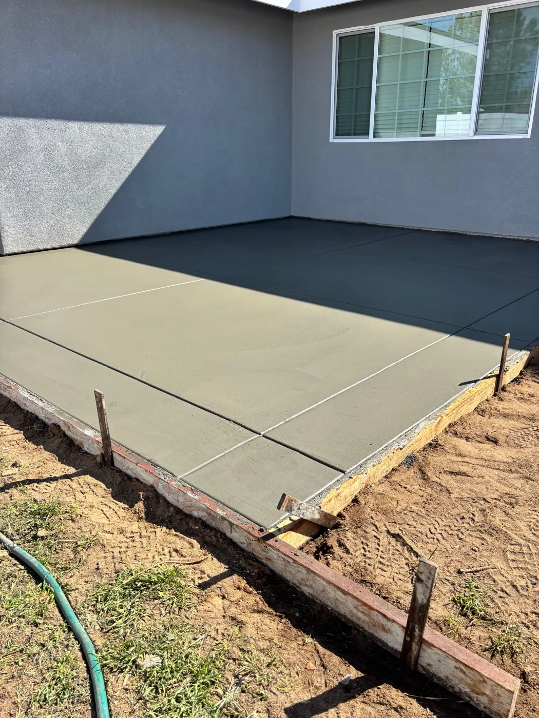 New concrete area beside a gray building with forms still at the edge