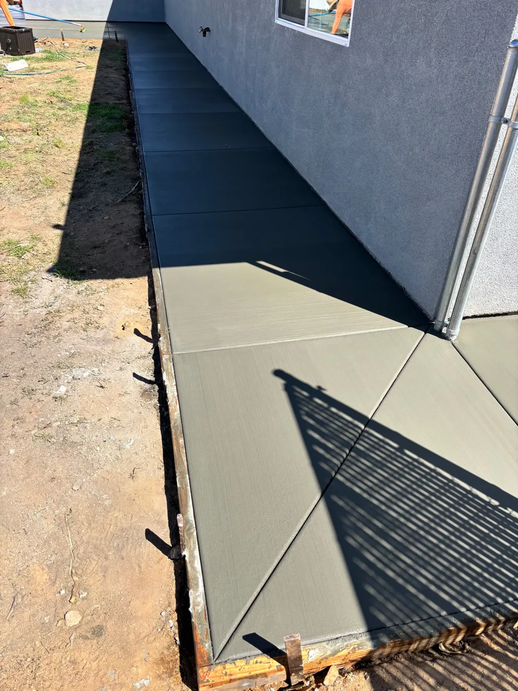 Finished concrete walkway following the exterior wall of a gray building
