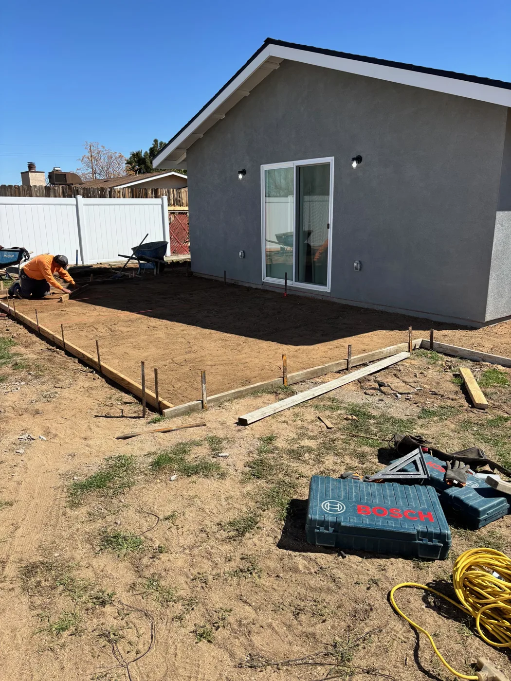 Timber forms and prepared soil beside a gray building