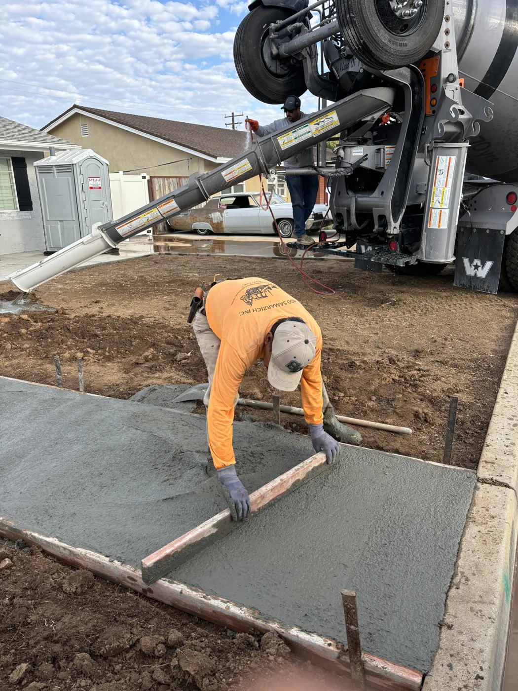 Worker finishing fresh concrete in a formed walkway beside the front yard