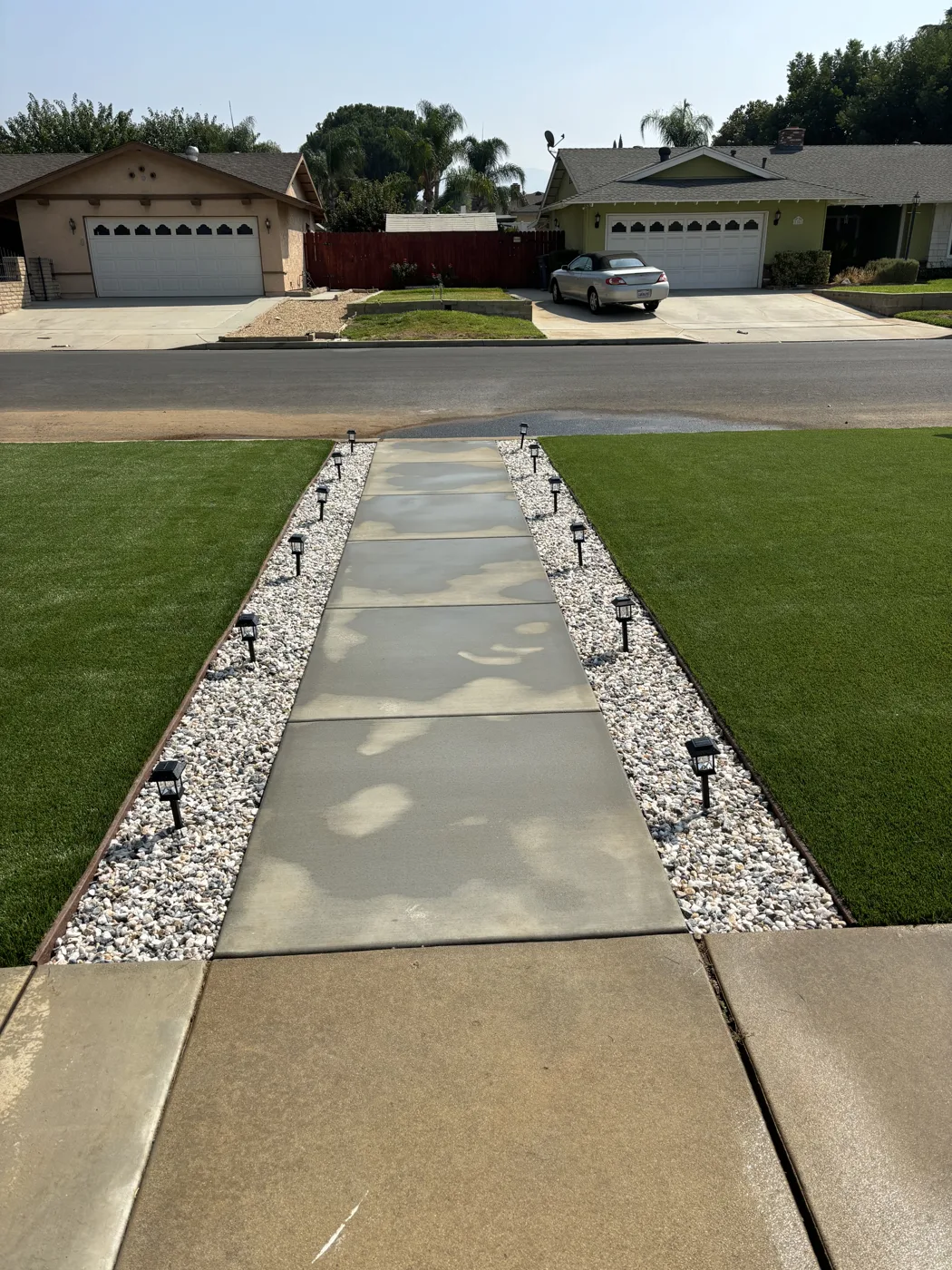 Straight concrete walkway with decorative stone borders between green lawn areas